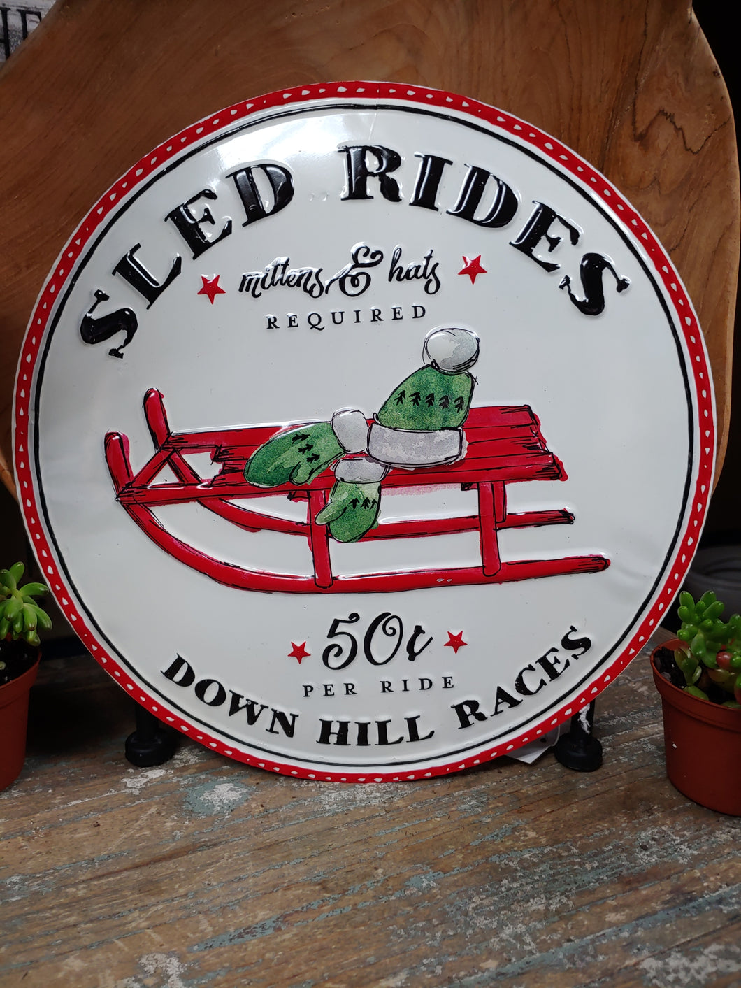 12”, ROUND, METAL/TIN CHRISTMAS SIGN. WHITE SIGN WITH RED TRIM AND SLED, AND GREEN AND WHITE MITTENS. WORDING, “SLED RIDES, MITTENS AND HATS REQUIRED,” “50¢ PER RIDE,” AND “DOWN HILL RIDES.” IT’S NEVER TOO EARLY FOR CHRISTMAS ITEMS.