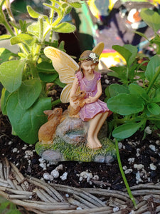 FAIRY GARDEN – RESIN – ‘SHARING SECRETS’ | MG286 | 3” TALL | CUTE FAIRY IN A PINK DRESS, YELLOW WINGS, GREEN VINE WITH WHITE FLOWER IN BROWN HAIR/2 BROWN BUNNIES BESIDE HER WHILE SHE SITS ON GREY-BROWN ROCK SHARING HER SECRETS WITH HER BUNNY FRIENDS/GREEN GRASS AND GREY STONES AT HER FEET.
