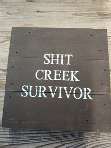 ‘SHIT CREEK SURVIVOR, ’ 6” BY 6”, HANDMADE, DARK FINISH, WOODEN SIGN. MADE BY ‘SECOND NATURE BY HAND’ FROM 100-YEAR OLD HOMES NOT BEING REPLACED. EACH IS UNIQUE.