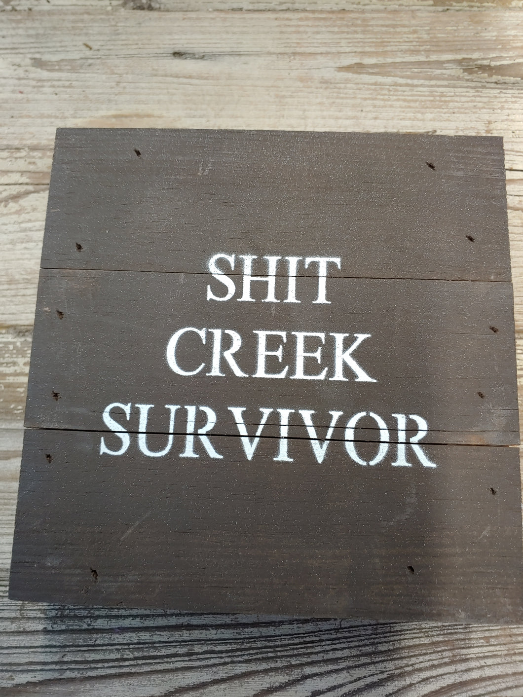 ‘SHIT CREEK SURVIVOR, ’ 6” BY 6”, HANDMADE, DARK FINISH, WOODEN SIGN. MADE BY ‘SECOND NATURE BY HAND’ FROM 100-YEAR OLD HOMES NOT BEING REPLACED. EACH IS UNIQUE.