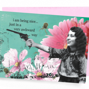 A GREETING CARD WITH PINK ENVELOPE. A TEAL BACKGROUND WITH PINK FLOWERS AND A DARK-HAIRED WOMAN, WEARING A RUFFLED BLOUSE AND AIMING A PISTOL. WORDS OUTSIDE – ‘I AM BEING NICE…JUST IN AN AWKWARD WAY.’ INSIDE: BLANK.