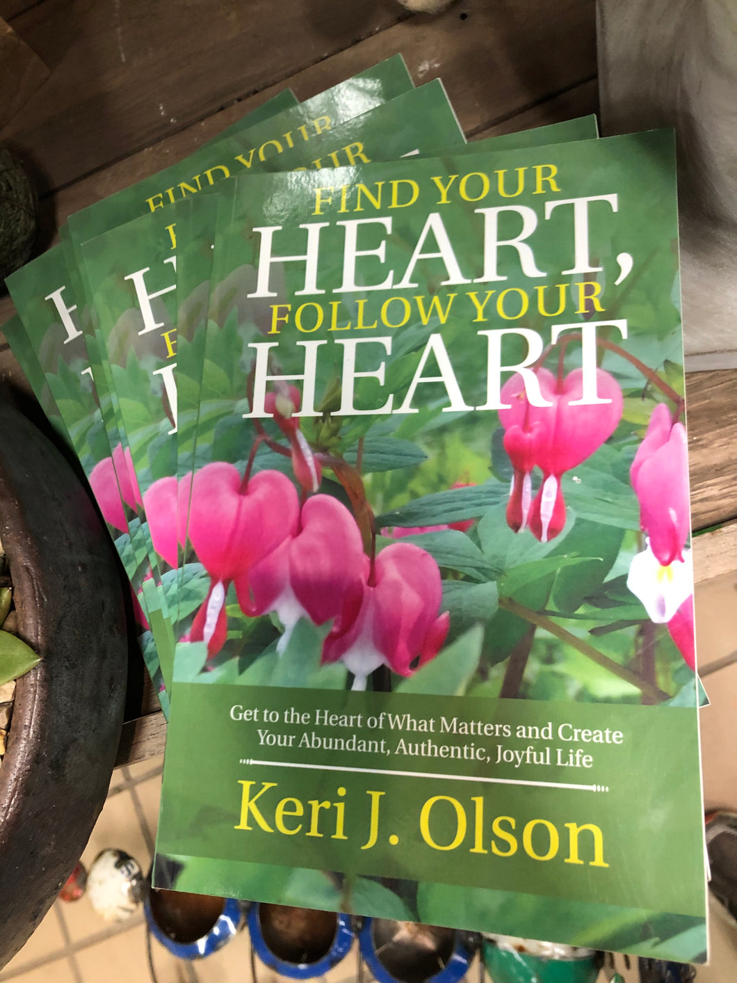 LARGE PAMPHLET ABOUT BLEEDING HEARTS BY KERI J OLSEN (SHE LIVES IN BARABOO!) | DARK GREEN BACKGROUND/WORDS IN YELLOW AND WHITE LETTERING/TOP: “FIND YOUR HEART, FOLLOW YOUR HEART” (HEART IS LARGE, WHITE FONT) | BOTTOM: WHITE “GET TO THE HEART OF WHAT MATTERS AND CREATE YOUR ABUNDANT, AUTHENTIC, JOYFUL LIFE”/WHITE DECORATIVE LINE/LARGE YELLOW WORDS KERI J OLSON | CENTER: BLEEDING HEARTS IN FULL BLOOM/DARK PINK HEARTS, RED-WHITE ‘BLOOD DROPS’ WITH DARK GREEN LEAVES.