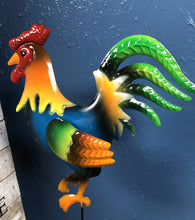 Load image into Gallery viewer, METAL ROOSTER 6 INCHES TALL BY 8 INCHES WIDE ON A METAL STAKE. COLORFUL WITH A RED HEAD, BLUE BODY, GREEN AND ORANGE WING, AND GREEN TAIL FEATHERS, AGAINST A BLUE WALL.