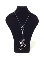 Load image into Gallery viewer, Hearts and Quatrefoils pendant necklace. The pendant has 3 silver-tone puffed hearts and 3 silver-tone quatrefoils that hang on varying lengths of black leather-like cords. The cords are attached to a silver-tone cap that hangs from the bottom of the neck cord. The necklace can easily slip over the head but does feature a lobster claw clasp with a 2&quot; chain extender