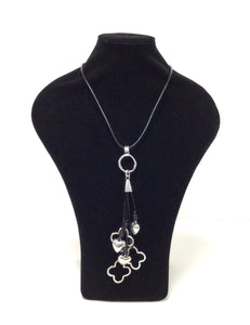 Hearts and Quatrefoils pendant necklace. The pendant has 3 silver-tone puffed hearts and 3 silver-tone quatrefoils that hang on varying lengths of black leather-like cords. The cords are attached to a silver-tone cap that hangs from the bottom of the neck cord. The necklace can easily slip over the head but does feature a lobster claw clasp with a 2" chain extender