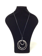 Load image into Gallery viewer, Three silver tone, mottled nested metal circles hang from a 18&quot;  leather like black cord small, med, large. Substantial statement piece. The largest circle is 3.25&quot;H x 3&quot;W. 