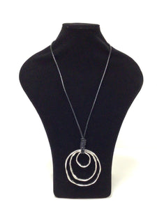 Three silver tone, mottled nested metal circles hang from a 18"  leather like black cord small, med, large. Substantial statement piece. The largest circle is 3.25"H x 3"W. 