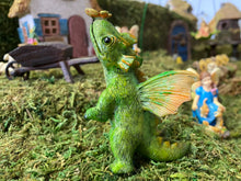 Load image into Gallery viewer, FAIRY GARDEN – RESIN – ‘LITTLE DRAGON’ FAIRY | MG305 | 3” T BY 2” W BY 2” D | 1” STAKE AT BOTTOM | GREEN SCALES/YELLOW-ORANGE WINGS/YELLOW-GREEN RIDGE-LINE SCALES | ON MOSS | ON BACK LEGS WITH YELLOW BUTTERFLY ON ITS NOSE | GREY WHEELBARROW IN BACKGROUND.