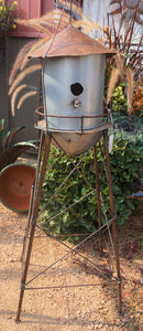 metal water tower bird house on long copper colored legs.  There is a deck around the base of the water tower with a copper cone-shaped roof.