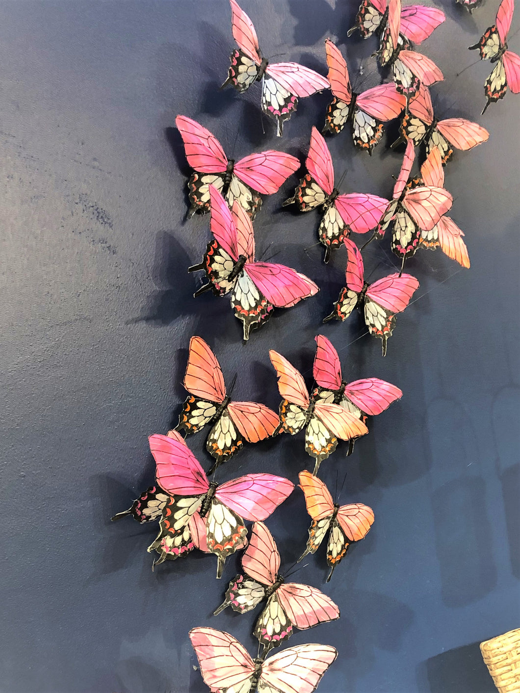 19 BUTTERFLY PICKS ON A DARK SURFACE MADE WITH FEATHERS. THEIR COLORS ARE ORANGE, BLUE, TAUPE, MAGENTA, PURPLE, AND GREEN. THEY ARE 4.5 INCHES HIGH BY 7 INCHES WIDE BY 1” DEEP AND COME WITH A 10” HIGH WIRE PICK.