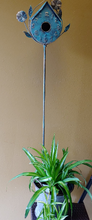 Load image into Gallery viewer, BLUE, PATINA COPPER BIRDHOUSE | ANTIQUE PATINA COPPER FINISH | CLOCK-STYLE PEAKED ROOF /ROUNDED BOTTOM AND PERCH BELOW 2” OPENING/WEATHER AND RUST-RESISTANT | CRAFTED OF METAL LEAVES, VINES, FLOWERS, AND BIRD. SHOWS WITH A METAL STAND IN A BUCKET OF GREEN FOLIAGE; IT IS 55” T.
