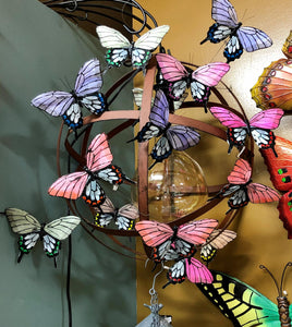 16 BUTTERFLY PICKS MADE WITH FEATHERS, ATTACHED TO A HANGING METAL BALL WITH A GLOBE HANGING INSIDE IT. THEIR COLORS ARE ORANGE, BLUE, TAUPE, MAGENTA, PURPLE, AND GREEN. THEY ARE 4.5 INCHES HIGH BY 7 INCHES WIDE BY 1” DEEP AND COME WITH A 10” HIGH WIRE PICK. THE BACKGROUND SHOWS A GREEN WALL ON THE LEFT AND A YELLOW WALL BEHIND.