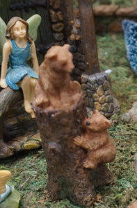 FAIRY GARDEN – 2 BEAR CUBS CLIMBING TREE STUMP. 1 SITTING ON TOP, OTHER CLIMBING | COLORS: CUBS ARE LIGHT BROWN; STUMP IS DARK BROWN. FAIRY GIRL WITH LIGHT GREEN WINDS, BROWN HAIR, LIGHT BLUE DRESS SITTING ON WALL WATCHIN CUBS.