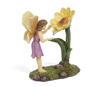 FAIRY WITH BROWN HAIR AND IN A PURPLE DRESS. | MG360 | STANDING ON MOSS LOOKING INTO A SMALL DAISY WITH YELLOW PETALS, AND ORANGE AND BROWN CENTER. DEW DROPS ARE FALLING FROM THE FLOWER. APPROXIMATELY 3.5" H BY 1.75" W BY 2.75" D.