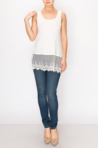 THE WOMAN HAS ON A LONG, WHITE TANK-TOP WITH A MATCHING CROCHETED HEM; IT HANGS BELOW HER WAIST. SHE HAS DARK BLUE SKINNY JEANS AND IVORY HIGH HEELS. S TO 2XL.