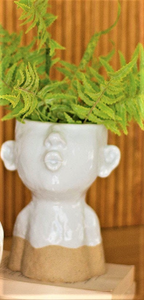 LARGE WHITE CERAMIC KISSING LADY HEAD PLANTER | 8.5” HIGH BY 6.25” WIDE | WHITE WITH SAND-COLORED BOTTOM | SITS ON 2 LIGHT TAN WOODEN BLOCKS WITH FERNS PLANTED IN IT | NOSE, EARS, AND PUCKERED MOUTH.