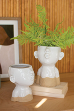 Load image into Gallery viewer, 2 LARGE WHITE CERAMIC KISSING LADY HEAD PLANTERS | 8.5” HIGH BY 6.25” WIDE | WHITE WITH SAND-COLORED BOTTOM | 1 SITS ON A WOODEN TABLE, 1 SITS ON 2 LIGHT TAN WOODEN BLOCKS WITH FERNS PLANTED IN IT | NOSE, EARS, AND PUCKERED MOUTH.